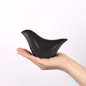 Minimalistische mattschwarze Vogelfigur für Heimdeko in der Hand auf weißem Grund