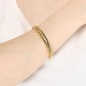 Detailed view of a gold-plated twisted wave bangle on wrist with a modern spiral texture