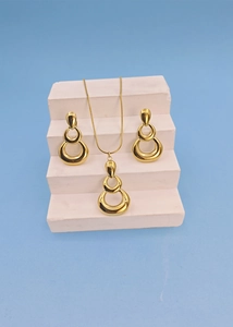 Golden geometric circle pendant necklace and hoop earring set on white pedestal