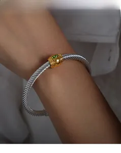 Detailed macro of a two-tone twisted cable bangle featuring a marquise green gemstone