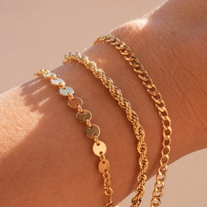 Gros plan de bracelets dorés en chaîne torsadée, à paillettes et gourmette au poignet