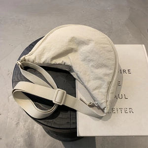 Detail of a beige crescent crossbody bag with adjustable strap on a minimalist wooden stool