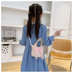 Detailed back view of a beige straw crossbody bag with a pink bow on a young girl
