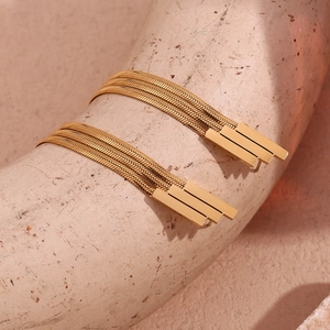 Macro shot of 18K gold plated tiered snake chain tassel earrings on a beige display stand
