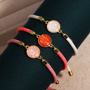 Detailed view of three braided rope bracelets with round resin charms and gold metal fittings