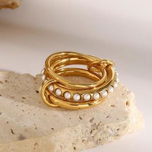 Stacked golden stainless steel ring with white pearls on elegant stone background