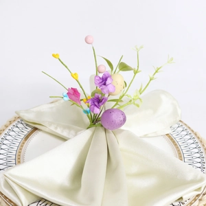 Easter napkin ring with purple eggs, artificial flowers, and green leaves on satin napkin