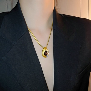Close-up of golden snake chain necklace with deep red teardrop stone and crystals