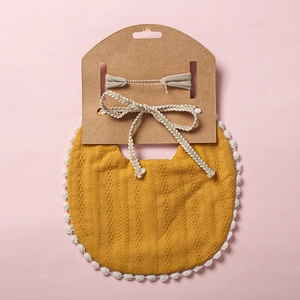 Détail de bavoir bébé tricoté jaune moutarde avec bordure en dentelle et noeud