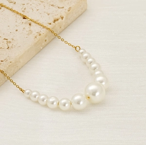 Detailed close-up of a graduated pearl necklace with a gold chain on a textured stone