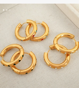 Détail de créoles dorées 18K avec zircons multicolores sur tissu de lin beige