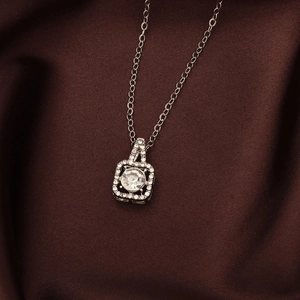 Elegant silver necklace featuring square pendant with round clear stone on dark silk