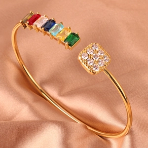 Detail van een gouden open armband met gekleurde zirkoon op zijden achtergrond