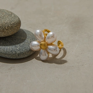 Close-up of a floral pearl ring with golden petals on elegant grey river stones
