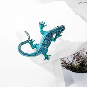 Detailed close-up of a sparkling lizard brooch with turquoise blue crystals on white stone