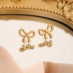 Boucles d'oreilles nœud dorées avec design ajouré sur miroir et tissu en satin