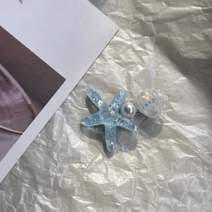 Close-up of blue sequin starfish, white pearl and shell hair clip on textured paper