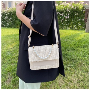 Detail of cream woven straw bag with decorative pearl chain and faux leather flap