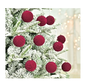 Close-up of red velvet Christmas balls with textured patterns on a snowy tree