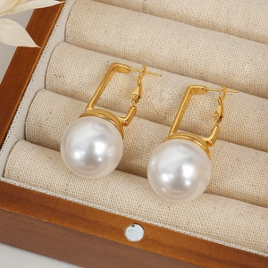 Boucles d'oreilles géométriques dorées avec grandes perles sur présentoir en bois