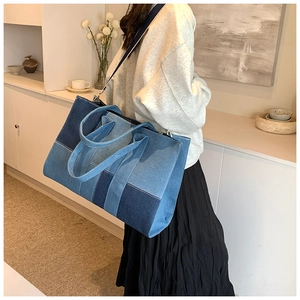 Detail of a large denim patchwork tote bag with an adjustable strap shown on a model