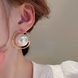Dettaglio di orecchini a perla dorati geometrici indossati da una modella in stile francese