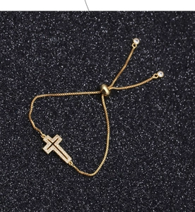 Macro detail of a gold cross bracelet with white cubic zirconia on a sparkling background