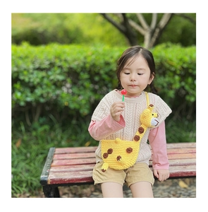 Detail of cute knitted giraffe crossbody bag worn by a young girl in an outdoor park setting