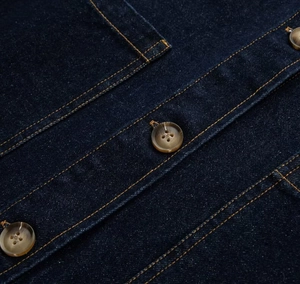 Détail macro de veste en jean bleu foncé avec boutons ambrés et coutures contrastées