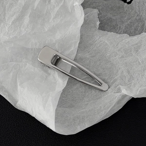 Macro detail of a silver-tone metal hair clip with polished finish on a textured background