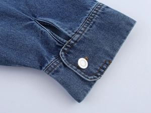 Close-up of denim jacket cuff showing blue twill fabric and silver metal button