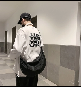 Detail of a black nylon dumpling messenger bag worn over a casual white graphic long sleeve