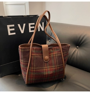 Detail of vintage plaid wool tote bag with brown leather handles on a leather sofa
