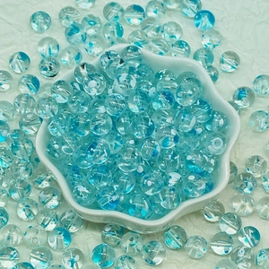 Macro shot of blue transparent glass beads with white floating flower patterns in a white bowl