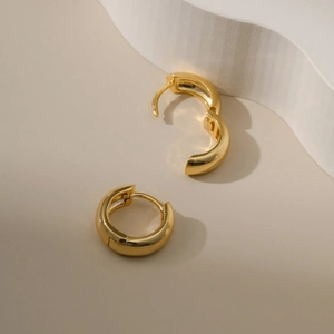 Polished 18K gold plated chunky hoop earrings on a minimalist beige background