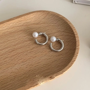 Macro detail of silver C-shaped pearl earrings on a minimalist oval wooden tray
