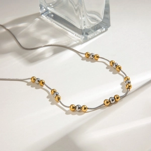 Two-tone stainless steel beaded necklace with gold and silver spheres on white surface