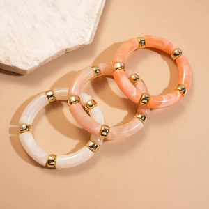 Détail de trois bracelets joncs en acrylique blanc, rose et orange avec anneaux en métal doré