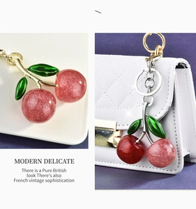 Detail showing two cherry keychains with glitter resin balls and green enamel leaves