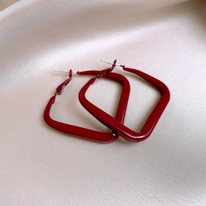 Close-up of red square hoop earrings with glossy finish on elegant champagne satin fabric
