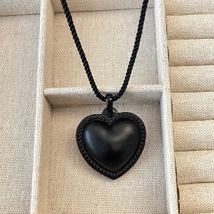 Collier cœur mat aux bords torsadés sur cordon noir posé sur fond de lin beige neutre
