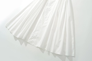 Dettaglio dell'orlo plissettato di un abito bianco su fondo bianco con ombre minimaliste