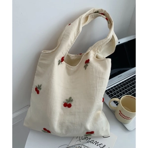 Detail of canvas tote bag featuring red cherry embroidery and wide handles on office desk