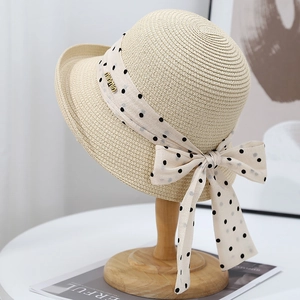Elegant wide-brim straw sun hat with polka dot ribbon and bow on a wooden stand