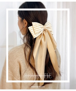 Rear view of a large champagne satin and plaid bow hair clip on model's wavy hair