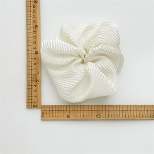 Glossy white oversized satin scrunchie with pleated texture shown with a ruler for scale