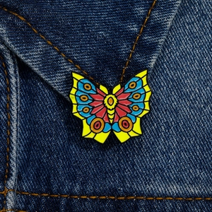 Colorful butterfly enamel pin badge on denim jacket collar showing vibrant wings