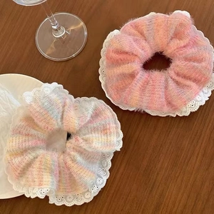 Detail of two colorful knit scrunchies with white lace trim on a dark wooden table