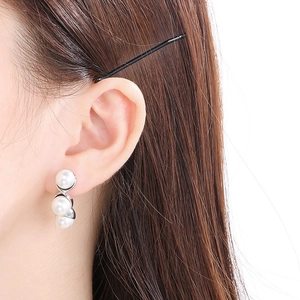 Close-up of elegant C-shaped silver earrings with three vertical pearls on model