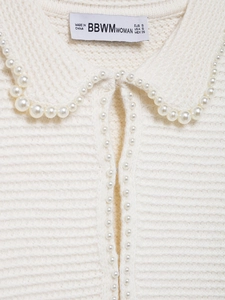 Gros plan du col de cardigan en maille blanche avec perles et texture de tricot côtelé